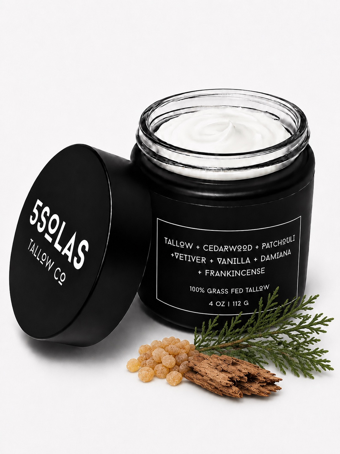 Open jar of 5Solas Tallow Co. grass‑fed tallow skin balm in the cedarwood + patchouli + vetiver + vanilla + damiana + frankincense blend, shown with natural ingredients around the container.